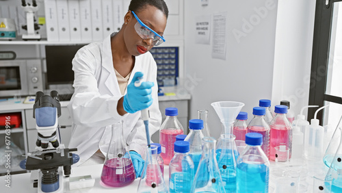 Black beauty in lab goggles, focused african american woman scientist firmly holds test tube, pouring liquid meticulously in bustling medical laboratory deep in concentration. photo