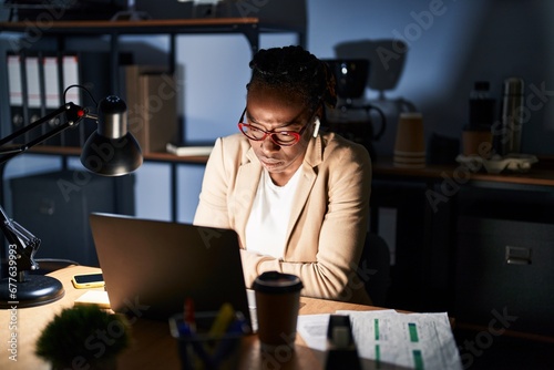 Beautiful black woman working at the office at night with hand on stomach because nausea, painful disease feeling unwell. ache concept.