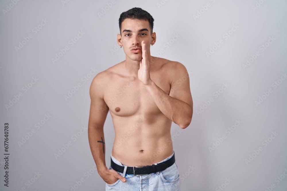 Handsome hispanic man standing shirtless hand on mouth telling secret rumor, whispering malicious talk conversation