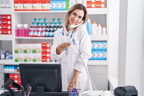 Young woman pharmacist talking on telephone reading prescription at pharmacy