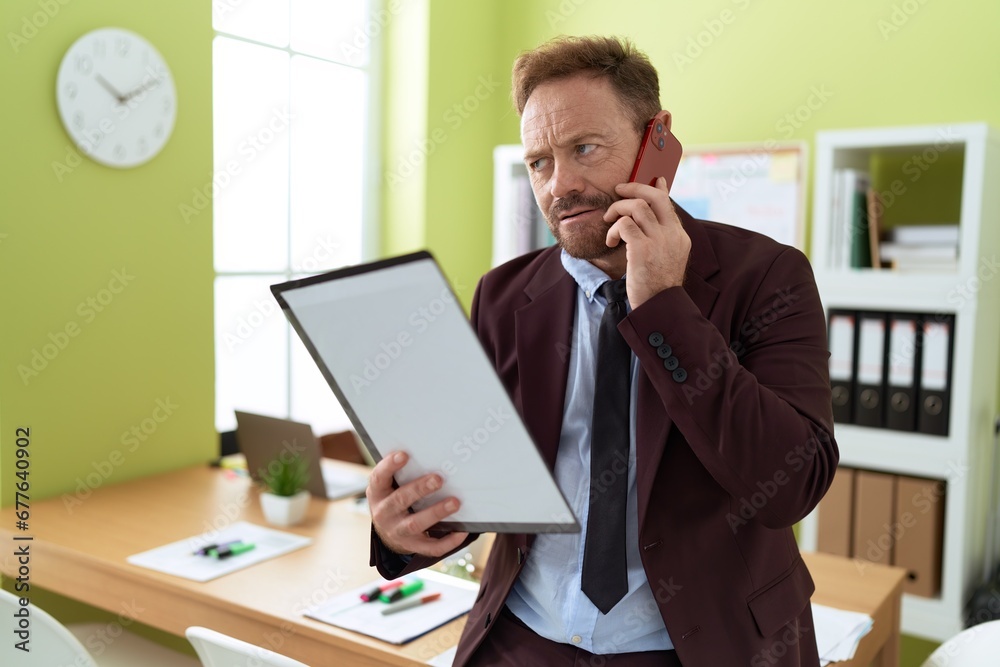 Middle age man business worker talking on smartphone reading document at office Middle age man business worker talking on smartphone reading document at office
