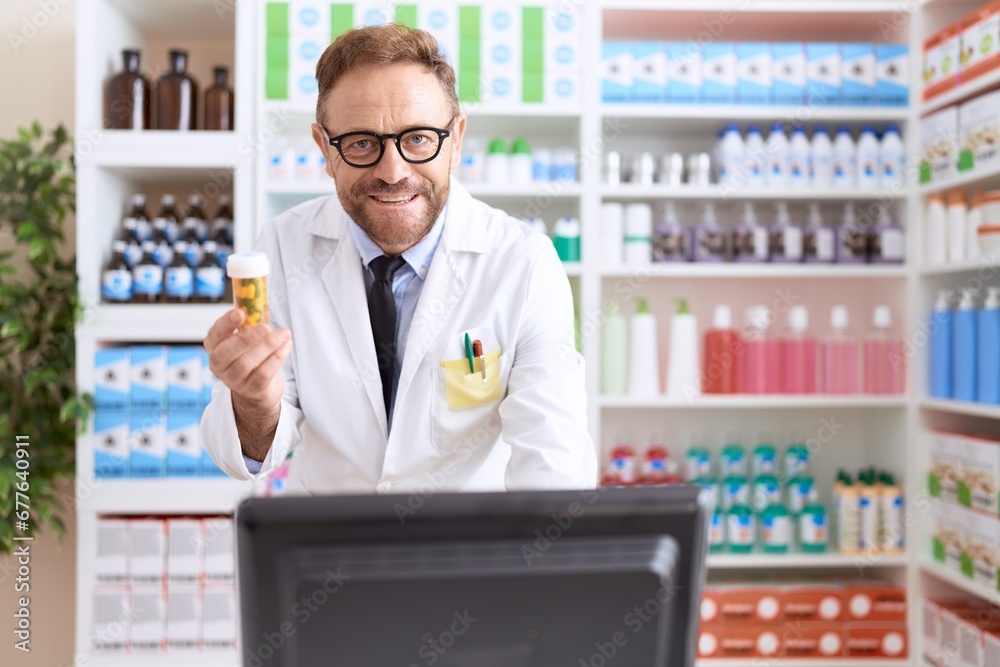 Middle age man pharmacist using computer holding pills bottle at pharmacy