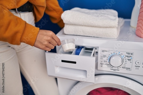 Young blonde woman pouring detergent on washing machine at laundry room
