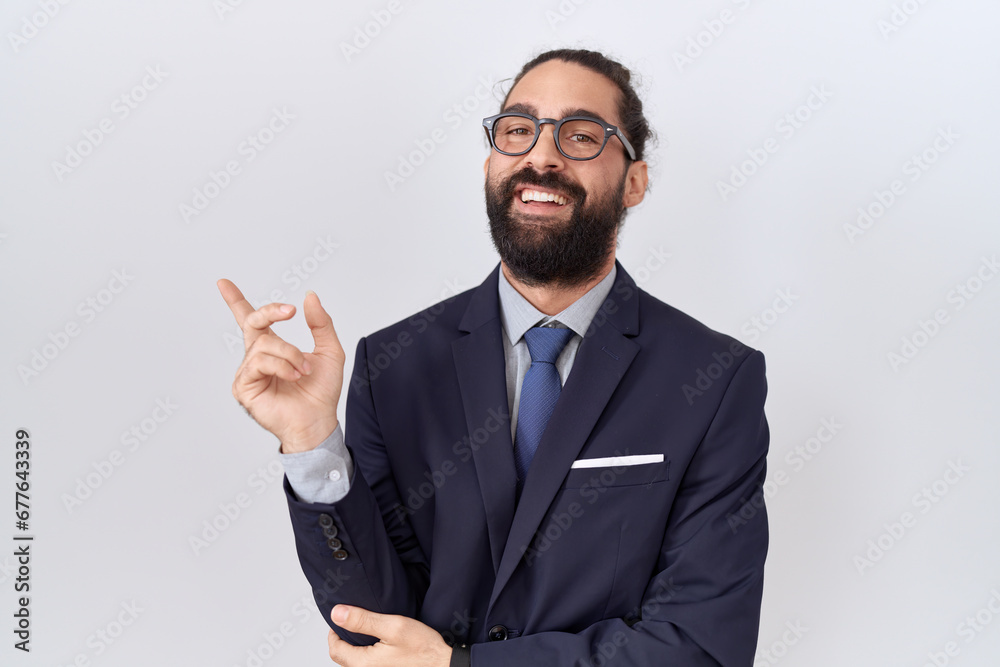 Hispanic man with beard wearing suit and tie with a big smile on face, pointing with hand and finger to the side looking at the camera. Hispanic man with beard wearing suit and tie with a big smile on face, pointing with hand and finger to the side looking at the camera.