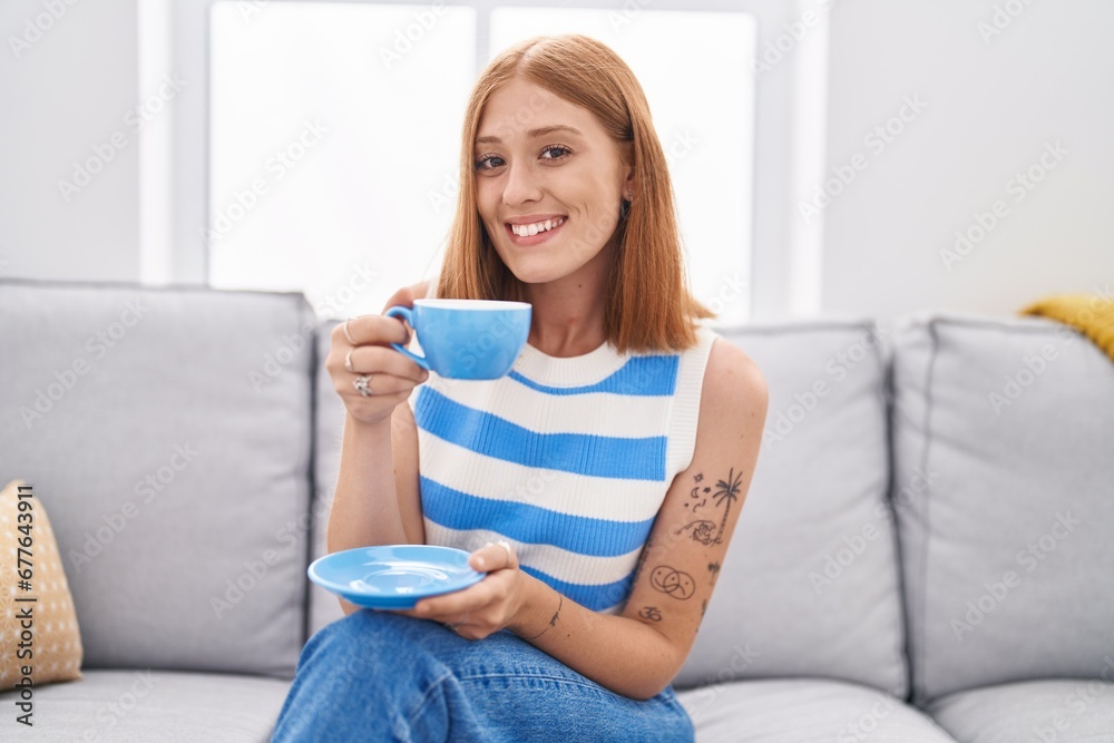 Young redhead woman drinking coffee sitting on sofa at home Young redhead woman drinking coffee sitting on sofa at home