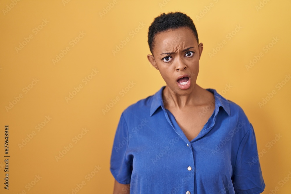 African american woman standing over yellow background in shock face, looking skeptical and sarcastic, surprised with open mouth African american woman standing over yellow background in shock face, looking skeptical and sarcastic, surprised with open mouth