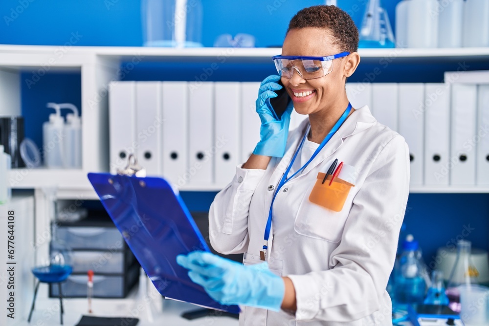 African american woman scientist talking on smartphone reading document at laboratory
