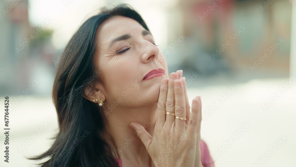 Middle age hispanic woman praying with closed eyes at street Middle age hispanic woman praying with closed eyes at street