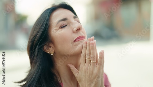 Middle age hispanic woman praying with closed eyes at street