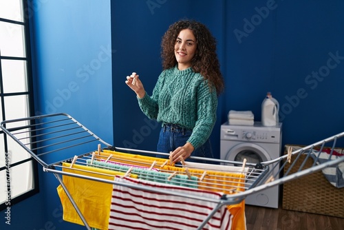 Young beautiful hispanic woman smiling confident hanging clothes on clothesline at laundry room