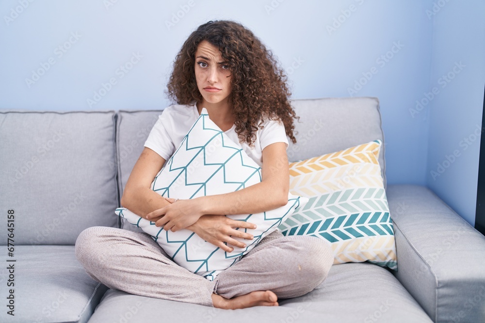 Hispanic woman with curly hair sitting on the sofa at home skeptic and nervous, frowning upset because of problem. negative person. Hispanic woman with curly hair sitting on the sofa at home skeptic and nervous, frowning upset because of problem. negative person.