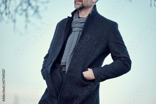 Man in a navy blue coat and a blue wool scarf, hand in pocket. Warm classic autumn winter men's clothing
