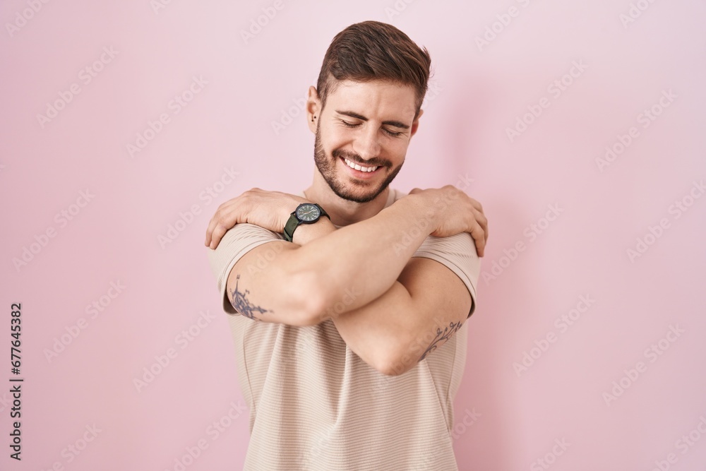 Hispanic man with beard standing over pink background hugging oneself happy and positive, smiling confident. self love and self care Hispanic man with beard standing over pink background hugging oneself happy and positive, smiling confident. self love and self care