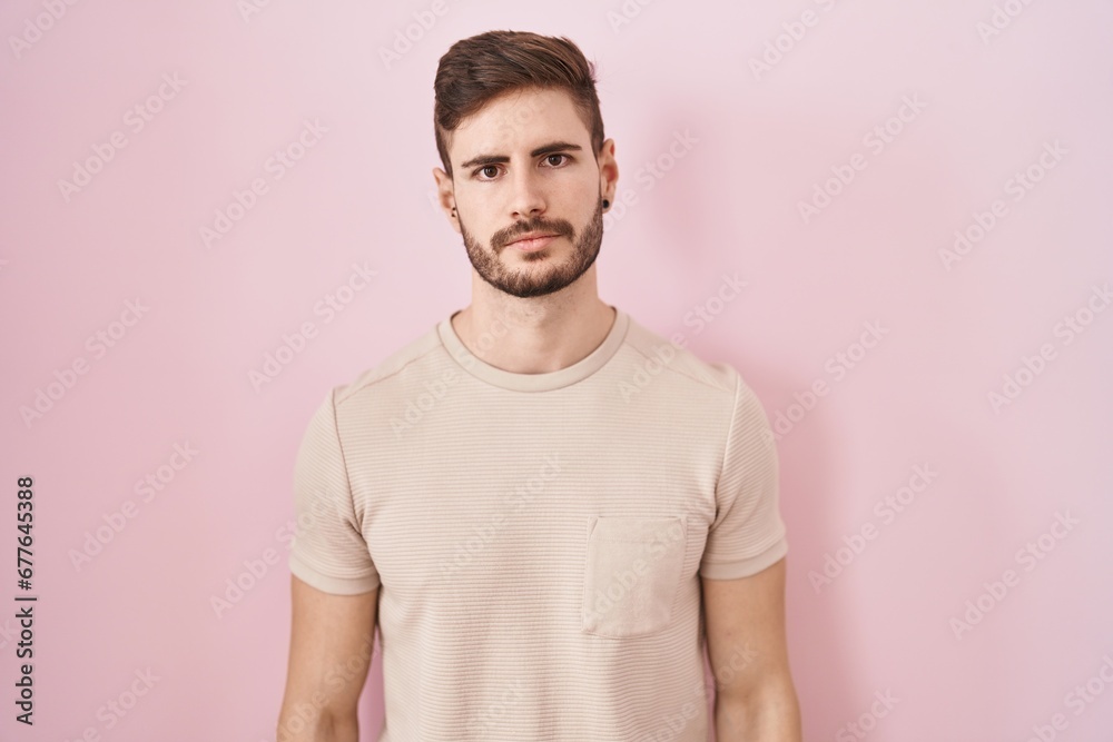 Hispanic man with beard standing over pink background relaxed with serious expression on face. simple and natural looking at the camera. Hispanic man with beard standing over pink background relaxed with serious expression on face. simple and natural looking at the camera.
