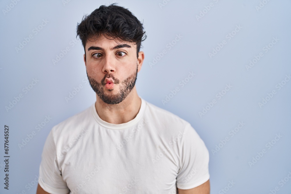 Hispanic man with beard standing over white background making fish face with lips, crazy and comical gesture. funny expression. Hispanic man with beard standing over white background making fish face with lips, crazy and comical gesture. funny expression.