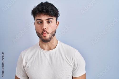 Hispanic man with beard standing over white background making fish face with lips, crazy and comical gesture. funny expression.