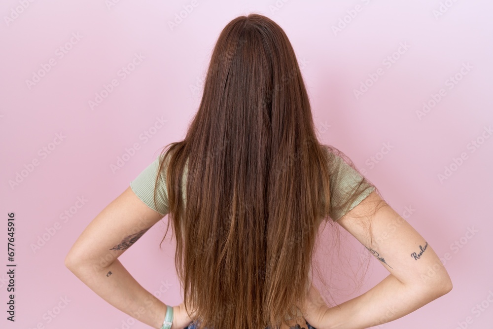 Beautiful brunette woman standing over pink background standing backwards looking away with arms on body Beautiful brunette woman standing over pink background standing backwards looking away with arms on body