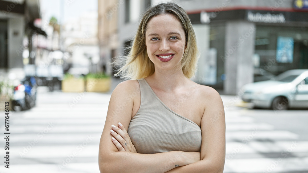 Young blonde woman smiling confident standing with arms crossed gesture at street