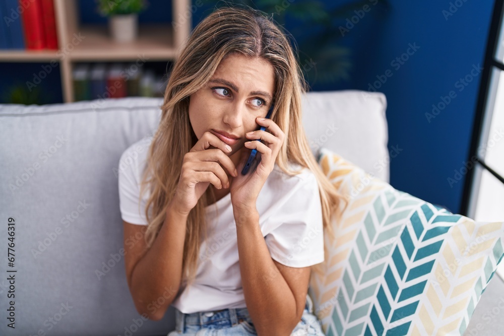 Young blonde woman talking on smartphone with worried expression at home Young blonde woman talking on smartphone with worried expression at home