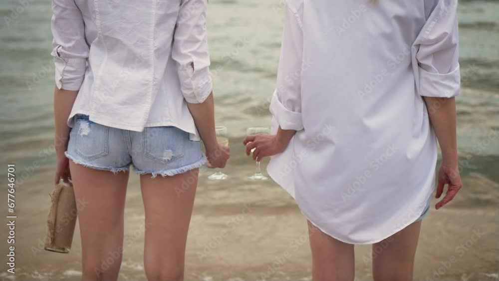 Unrecognizable Lesbian women couple on beach holding glasses with white wine, standing in waves, LGBT lovers celebrating marriage and honeymoon together. Event, LGBT Pride Month, friendship concept Unrecognizable Lesbian women couple on beach holding glasses with white wine, standing in waves, LGBT lovers celebrating marriage and honeymoon together. Event, LGBT Pride Month, friendship concept