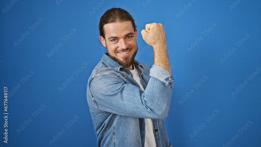 Fototapeta premium Young hispanic man smiling confident doing strong gesture with arm over isolated blue background