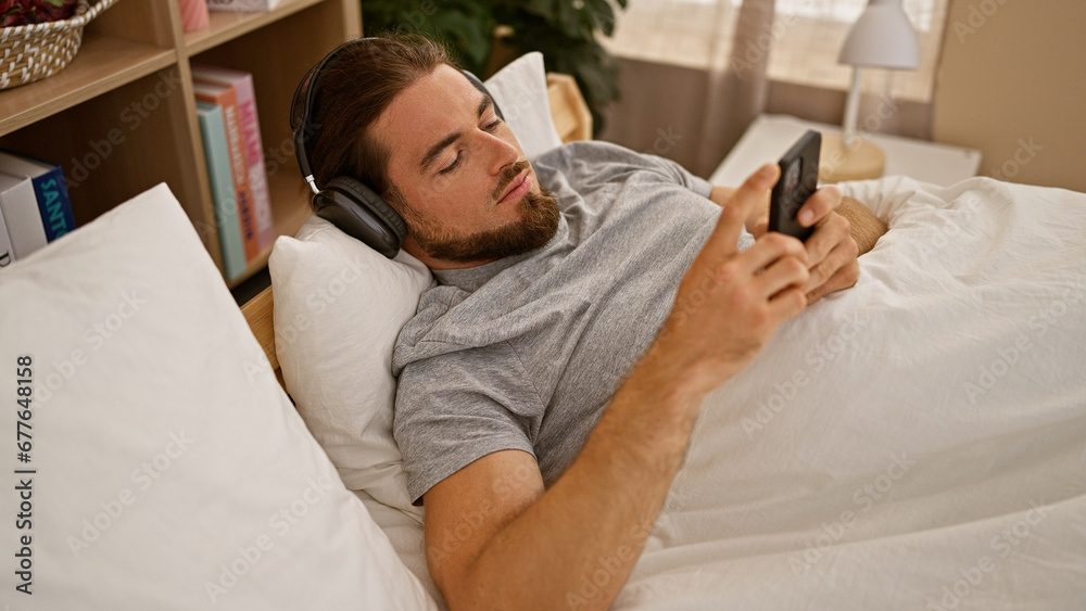 Young hispanic man using smartphone lying on the bed wearing headphones at bedroom Young hispanic man using smartphone lying on the bed wearing headphones at bedroom