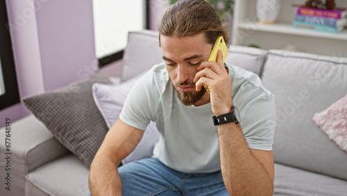 Young hispanic man speaking on the phone sitting on sofa at home