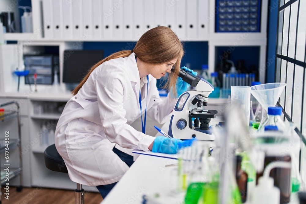 Young caucasian woman scientist using microscope write on document at laboratory Young caucasian woman scientist using microscope write on document at laboratory
