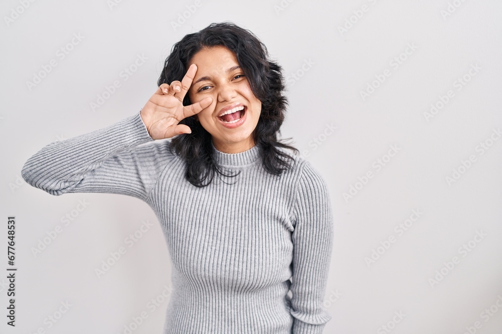 Hispanic woman with dark hair standing over isolated background doing peace symbol with fingers over face, smiling cheerful showing victory Hispanic woman with dark hair standing over isolated background doing peace symbol with fingers over face, smiling cheerful showing victory