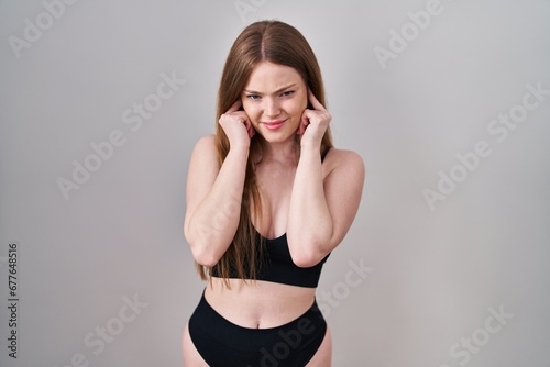 Young caucasian woman wearing lingerie covering ears with fingers with annoyed expression for the noise of loud music. deaf concept. © Krakenimages.com