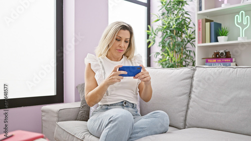 Young blonde woman watching video on smartphone sitting on sofa with serious face at home