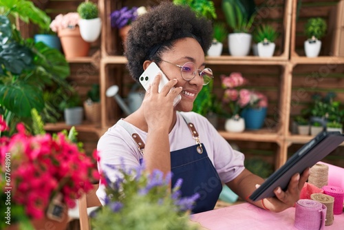 African american woman florist talking on smartphone using touchpad at flower shop