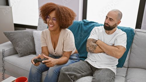 Beautiful interracial couple, looking upset, sit together at home playing video game - love connection tested in living room! photo