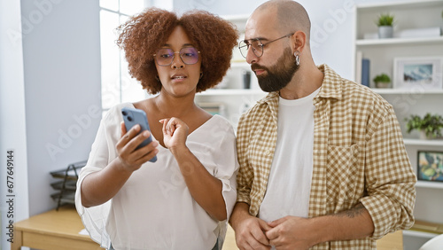 Two focused workers, one man and one woman, working together on a smartphone at the office while standing indoors concentrating for business success