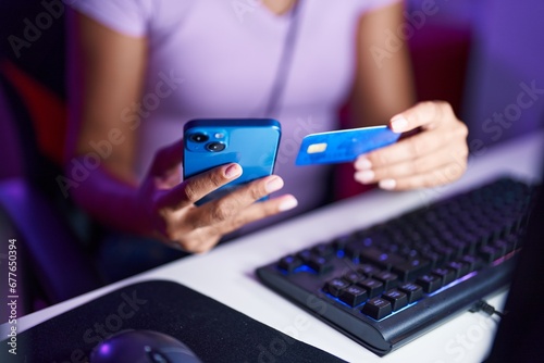 Young beautiful hispanic woman using smartphone and credit card at gaming room