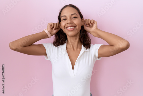 Young hispanic woman wearing casual white t shirt smiling pulling ears with fingers, funny gesture. audition problem photo