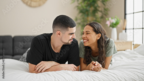 Happy love blooming in the beautiful couple's room as they enjoy a relaxed morning, lying in bed, smiling & looking at each other in their comfortable bedroom.