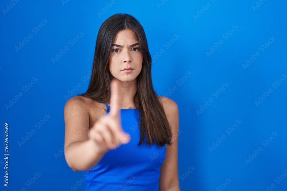 Hispanic woman standing over blue background pointing with finger up and angry expression, showing no gesture Hispanic woman standing over blue background pointing with finger up and angry expression, showing no gesture