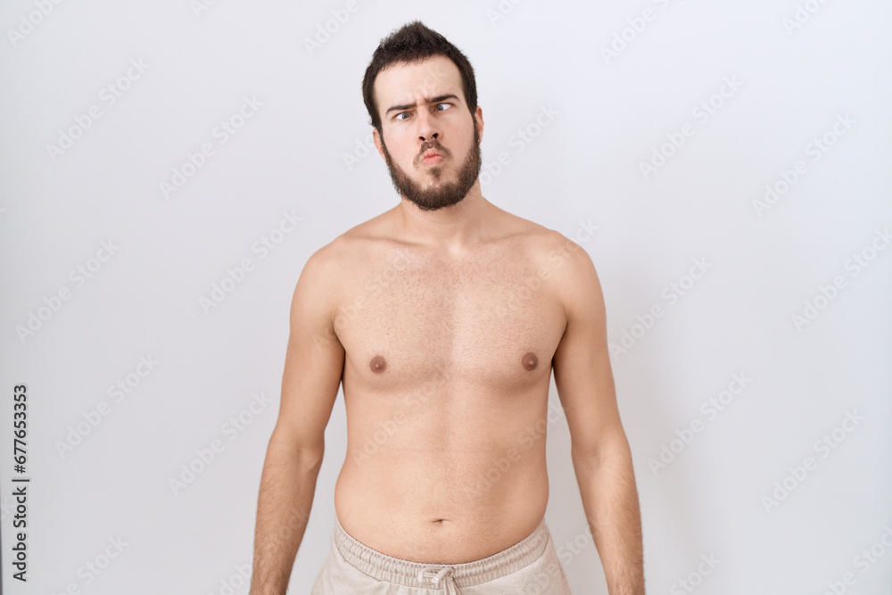 Young hispanic man standing shirtless over white background making fish face with lips, crazy and comical gesture. funny expression.