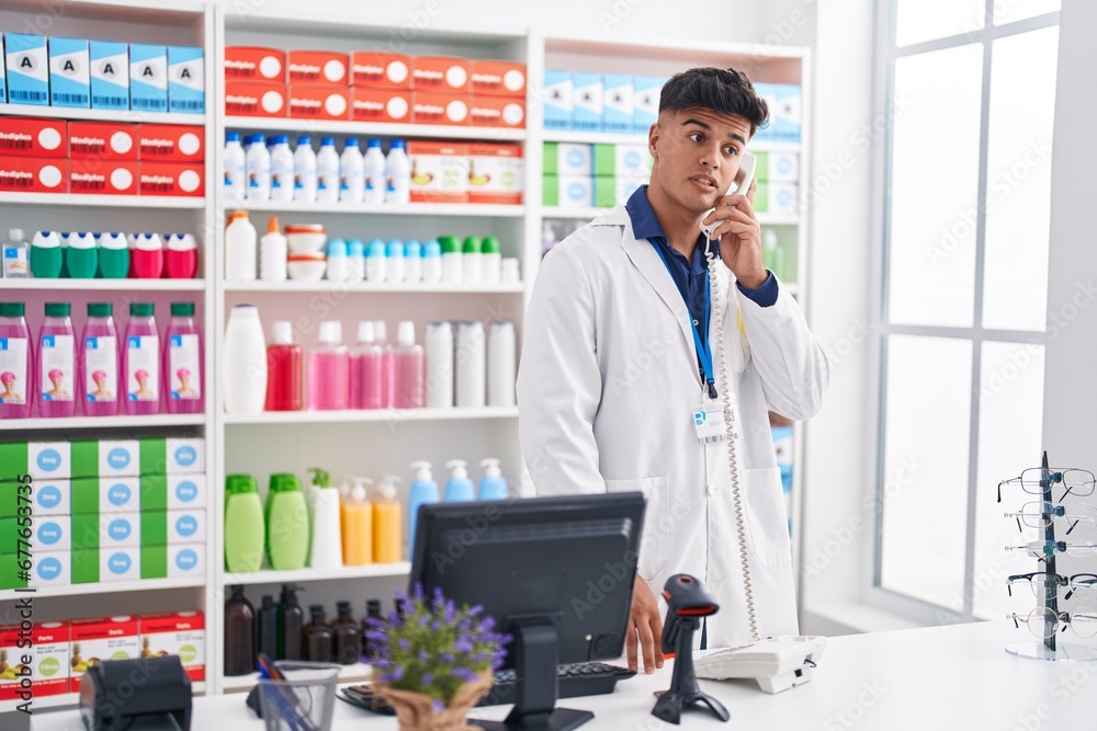 Young hispanic man pharmacist talking on telephone at pharmacy Young hispanic man pharmacist talking on telephone at pharmacy