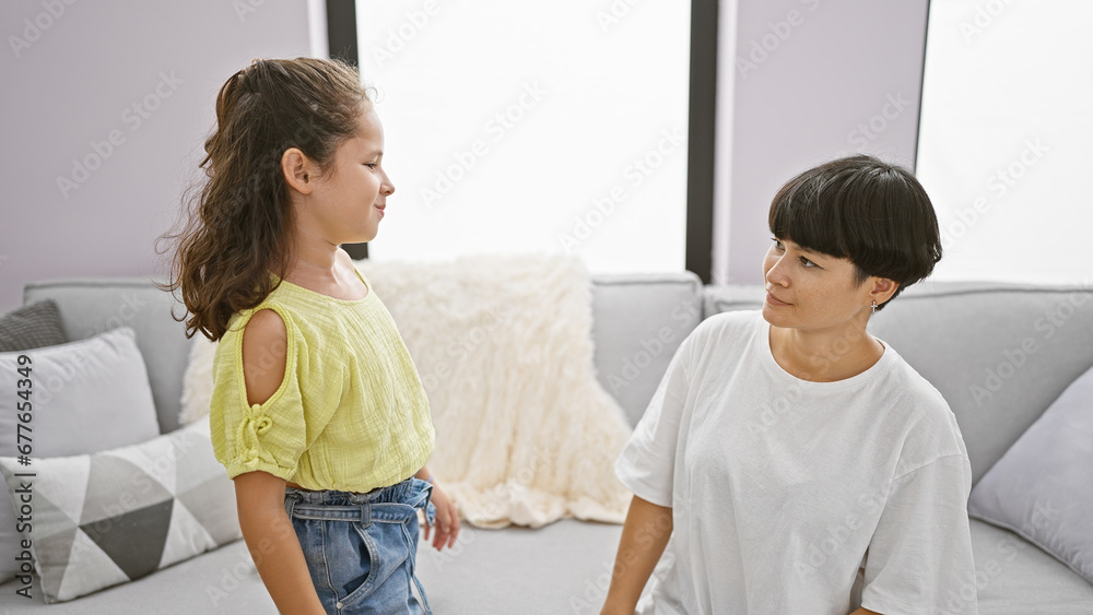 Obraz premium Mother and daughter sitting on sofa looking each other at home