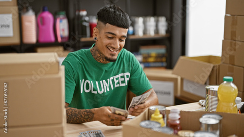 Confident young latin man volunteer, smiling while counting dollars at charity center, making a difference
