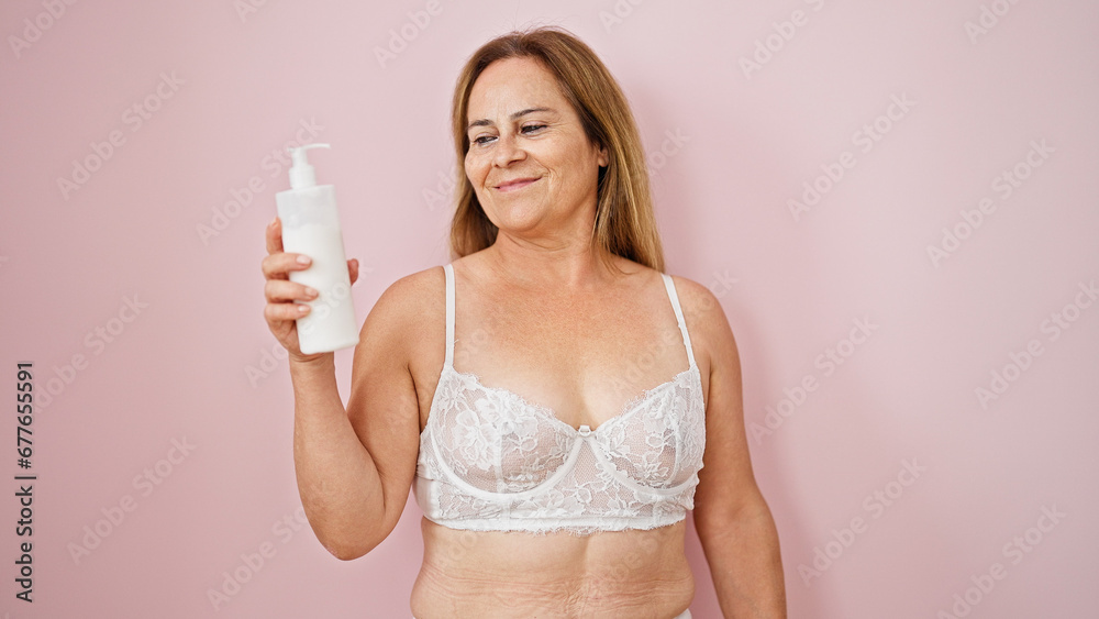 Middle age hispanic woman wearing lingerie holding lotion bottle over isolated pink background Middle age hispanic woman wearing lingerie holding lotion bottle over isolated pink background