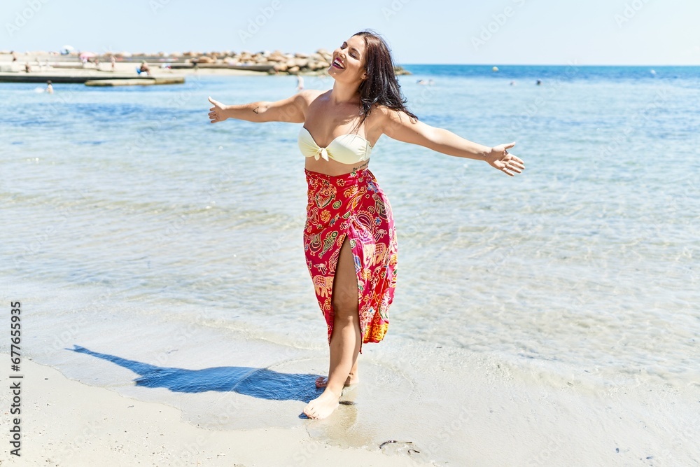 Young beautiful hispanic woman tourist wearing bikini with arms open at seaside Young beautiful hispanic woman tourist wearing bikini with arms open at seaside