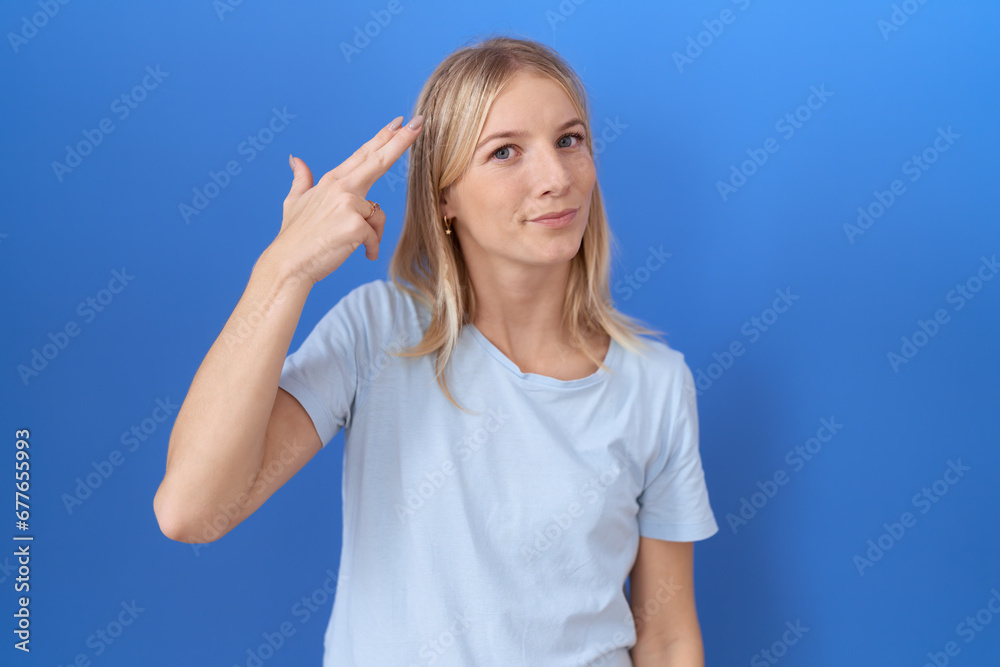 Young caucasian woman wearing casual blue t shirt shooting and killing oneself pointing hand and fingers to head like gun, suicide gesture. Young caucasian woman wearing casual blue t shirt shooting and killing oneself pointing hand and fingers to head like gun, suicide gesture.