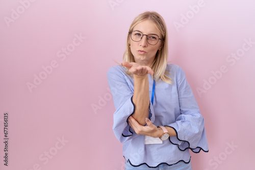 Young caucasian business woman wearing id card looking at the camera blowing a kiss with hand on air being lovely and sexy. love expression.