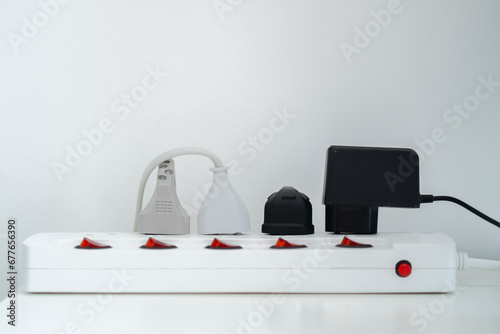 Many electrical plugs connected to a power white strip or extension block on wooden table