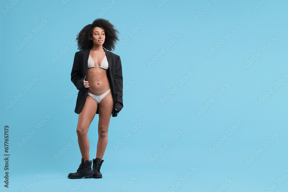 Fototapeta premium Beautiful woman in stylish bikini and jacket on light blue background, space for text