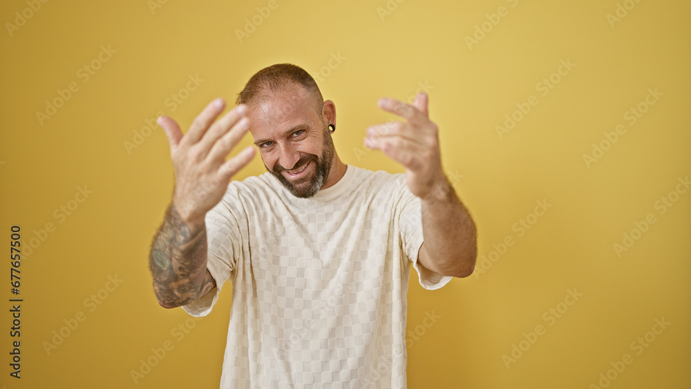 Fototapeta premium Happy young man, exuding confidence, flashing a cool smile and coming gesture with hands isolated on a vibrant yellow background