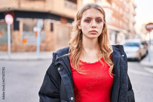 Young blonde woman standing with serious expression at street